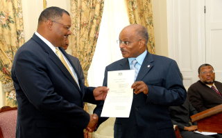 Governor-General, His Excellency the Most Hon. Professor Kenneth Hall (right), presents the instrument of appointment to Director of Elections, Danville Walker (left), at an official ceremony at King's House. Seated in the background is Minister of National Security, Dr. Peter Phillips.