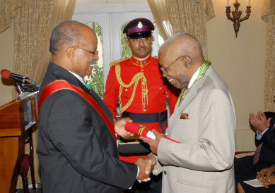 Governor General, His Excellency, The Most Hon. Professor Sir Kenneth Hall (left) presents Professor Charles Egerton Denbow with the instrument of the Order of Distinction in the Rank of Commander during a special ceremony of investiture at King's House on Wednesday (April 16). Professor Denbow was presented with the award in recognition of his outstanding work in the field of medicine and in particular, the teaching of medicine. Looking on is Captain Samuel Ellis, Aid-de-Camp to the Governor General.