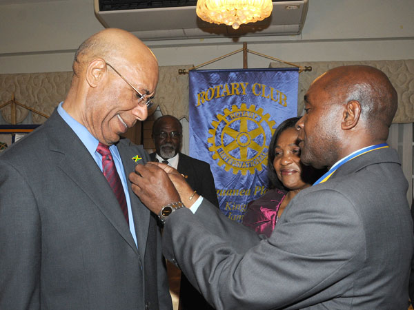 Governor-General, His Excellency the Most Hon. Sir Patrick Allen (left), seems very pleased as President of the Rotary Club of Liguanea Plains, Mrs. Astley Jones, affixes the Rotary Club pin to the Governor-General’s lapel. Occasion was a Club meeting, held at Eden Gardens, in Kingston, on September. 10, at which the Governor-General  was inducted as an Honorary Rotarian. Looking on (partially hidden) is the Governor-General’s wife,  Lady Allen.