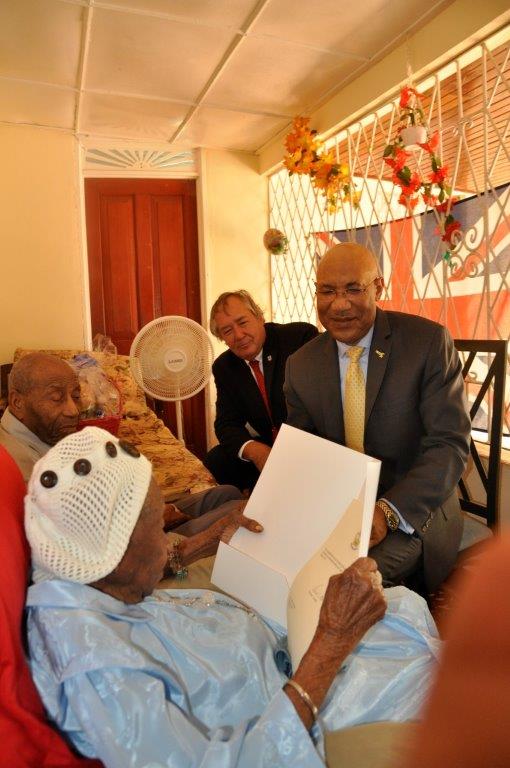 Ms. Vioris Brown reads congratulatory Tribute presented to her by His Excellency The Governor-General. Looking on are the Hon. Paul Muschette Custos of Trelawny (left of the Governor-General) and Mr. Fairweather her son.