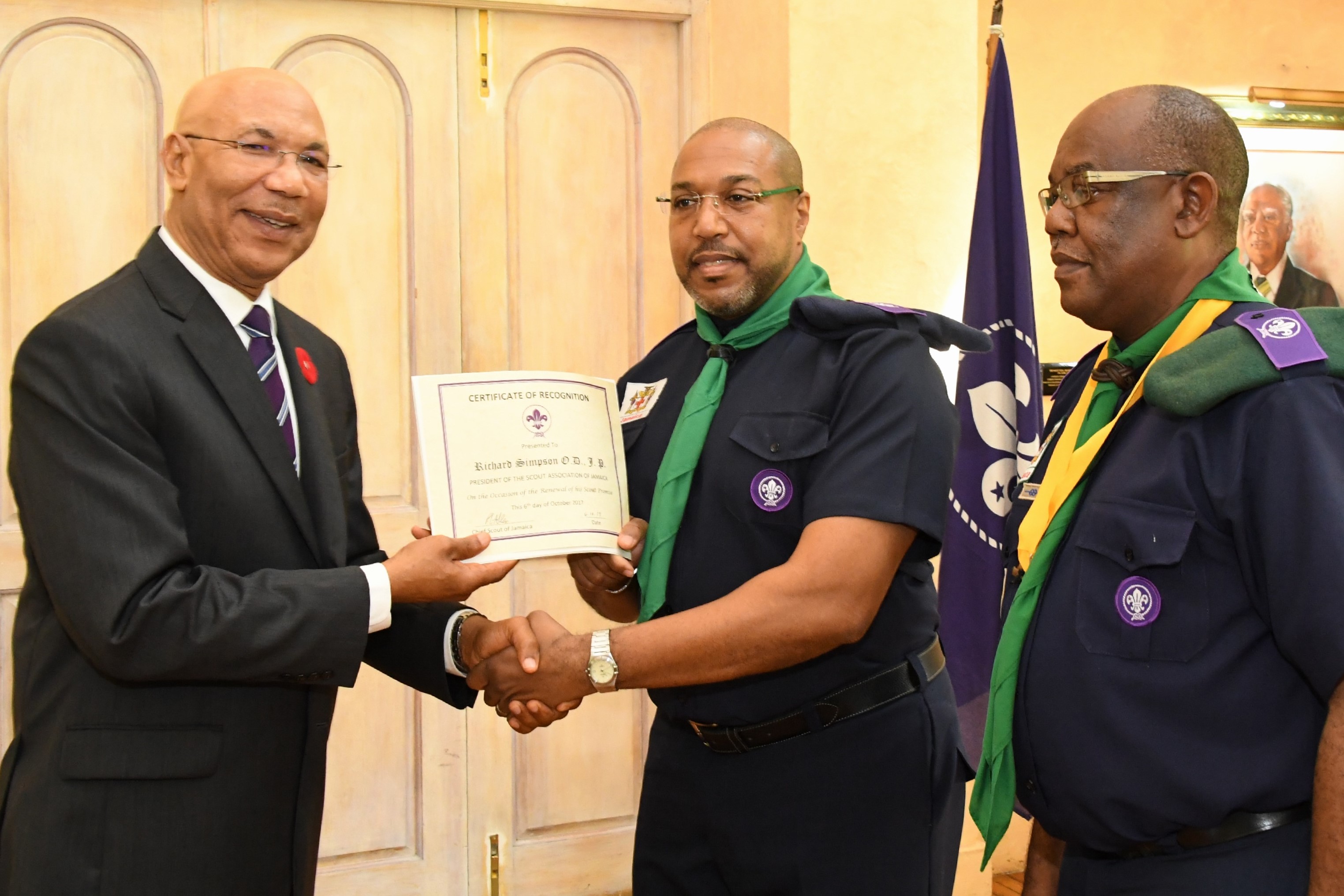 Governor-General Sir Patrick Allen (left) presents Mr. Richard Simpson with his certificate of appointment as the new President of the Scout Association of Jamaica.  Looking on is Mr. Maurice Brown Chief Commissioner.  